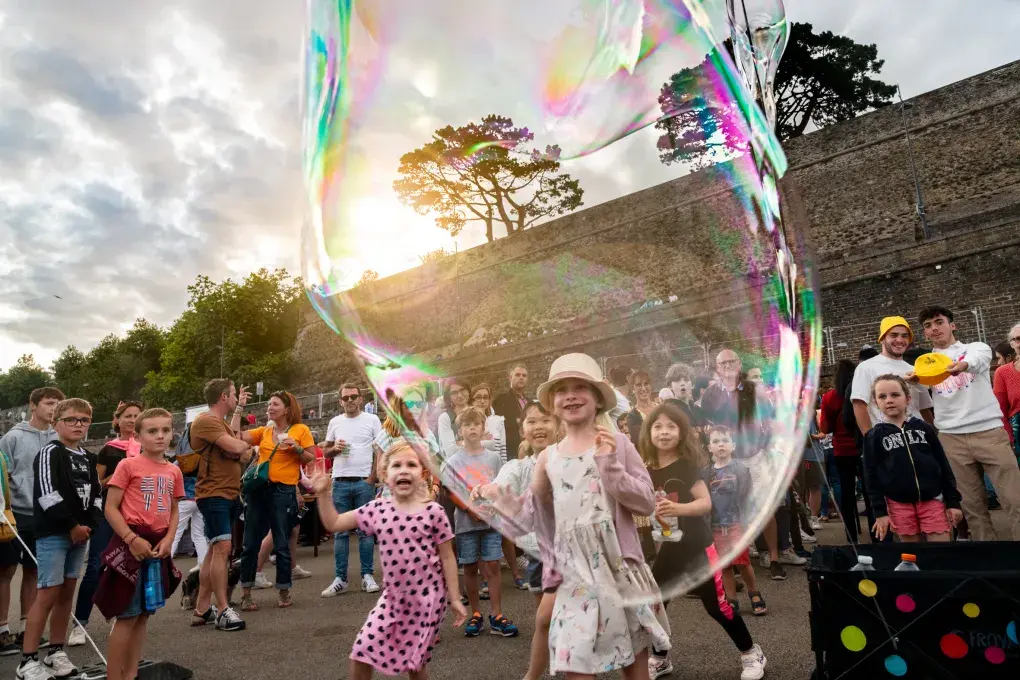 Des enfants rient devant un spectacle de bulles géantes. 