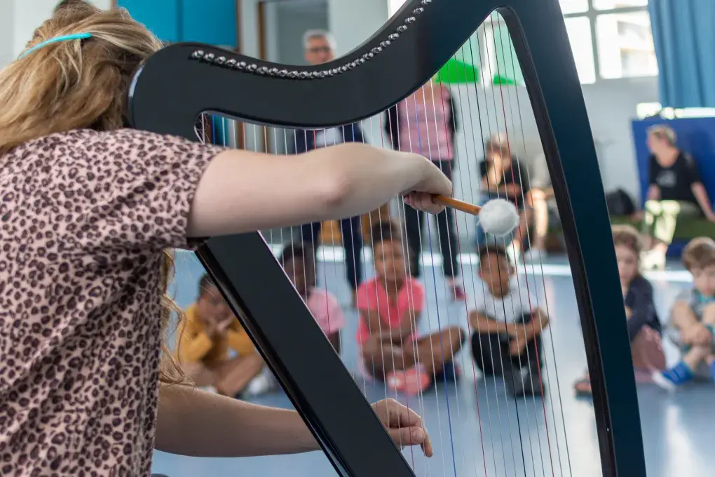 Une femme joue de la harpe devant des enfants. 