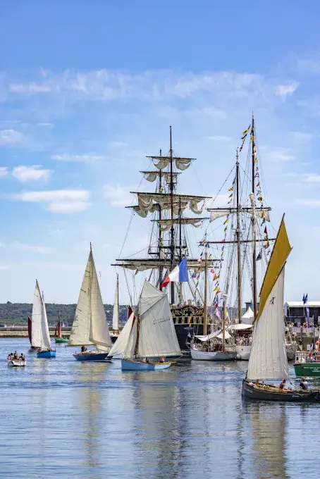 Des petits bateaux naviguent à côté d'immenses voiliers. 