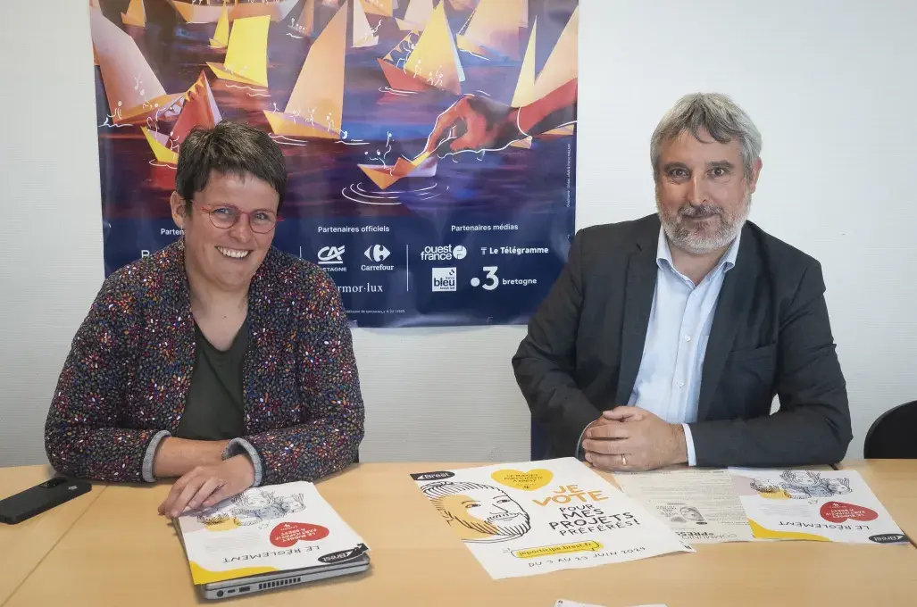 Deux personnes posent devant des affiches. 