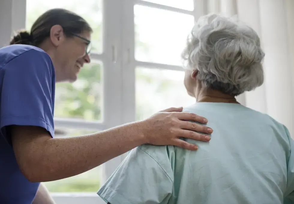 Une infirmière se penche en souriant vers une personne âgée