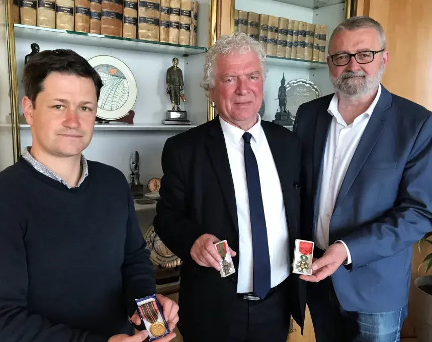 Trois hommes montrent les médailles attribuées à la ville de Brest suite à la Seconde Guerre mondiale