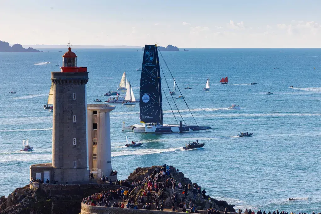 Un bateau géant passe devant un phare.