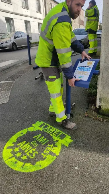 Un agent de la voire installe un assis-debout sur un poteau de signalisation 
