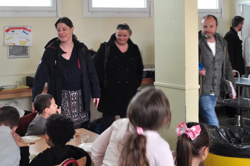 Des enfants assis à la cantine et des adultes autour leur parlant