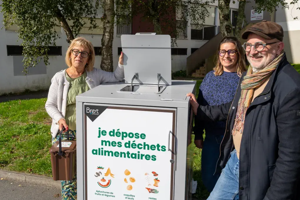 Trois personnes à côté d'un container à poubelles.