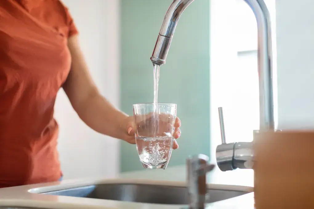 Une femme se sert un verre d'eau au robinet