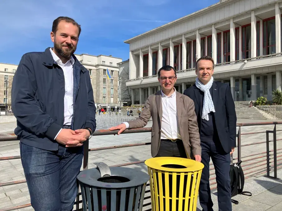 Trois hommes posent à côté de nouvelles corbeilles de tri des emballages, place de la Liberté