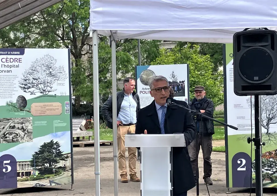 Un homme au micro, devant une exposition en plein air 