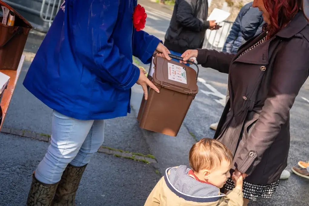 Deux personnes échangent un seau de déchets.