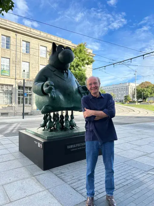 Philippe Geluck debout devant une de ses statues du Chat.