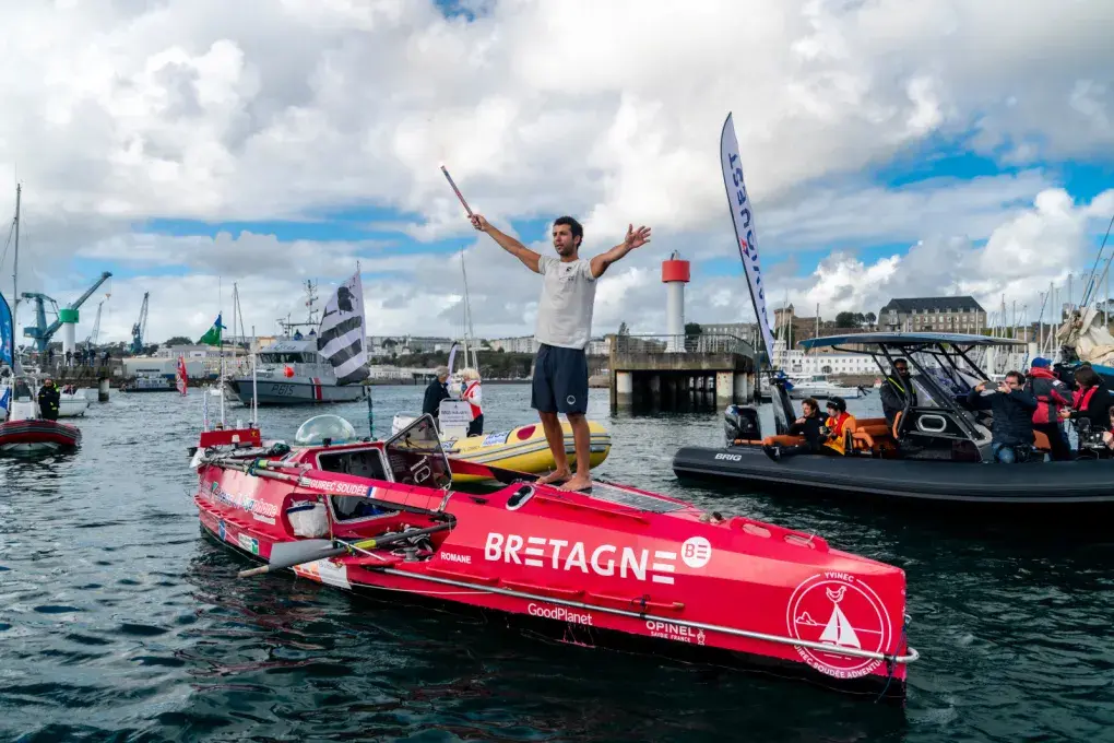 Un hommes les bras levé sur son aviron de mer arrivant au port de Brest devant une foule sur le quai