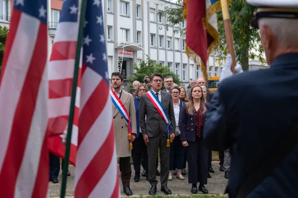 Trois personnes debout devant des drapeaux américains.