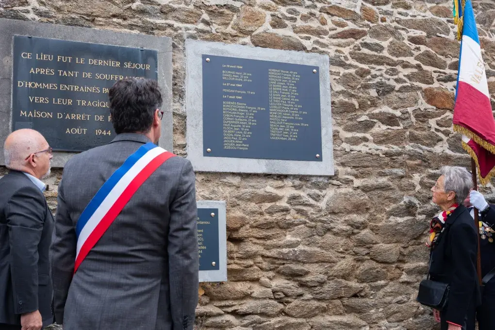 Trois personnes se tiennent devant des plaques commémoratives.