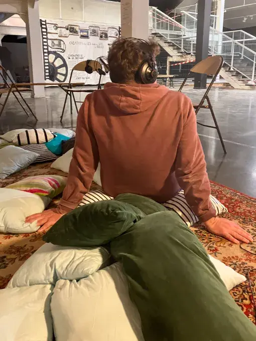 une jeune homme de dos, assis sur des coussins et un casque sur les oreilles