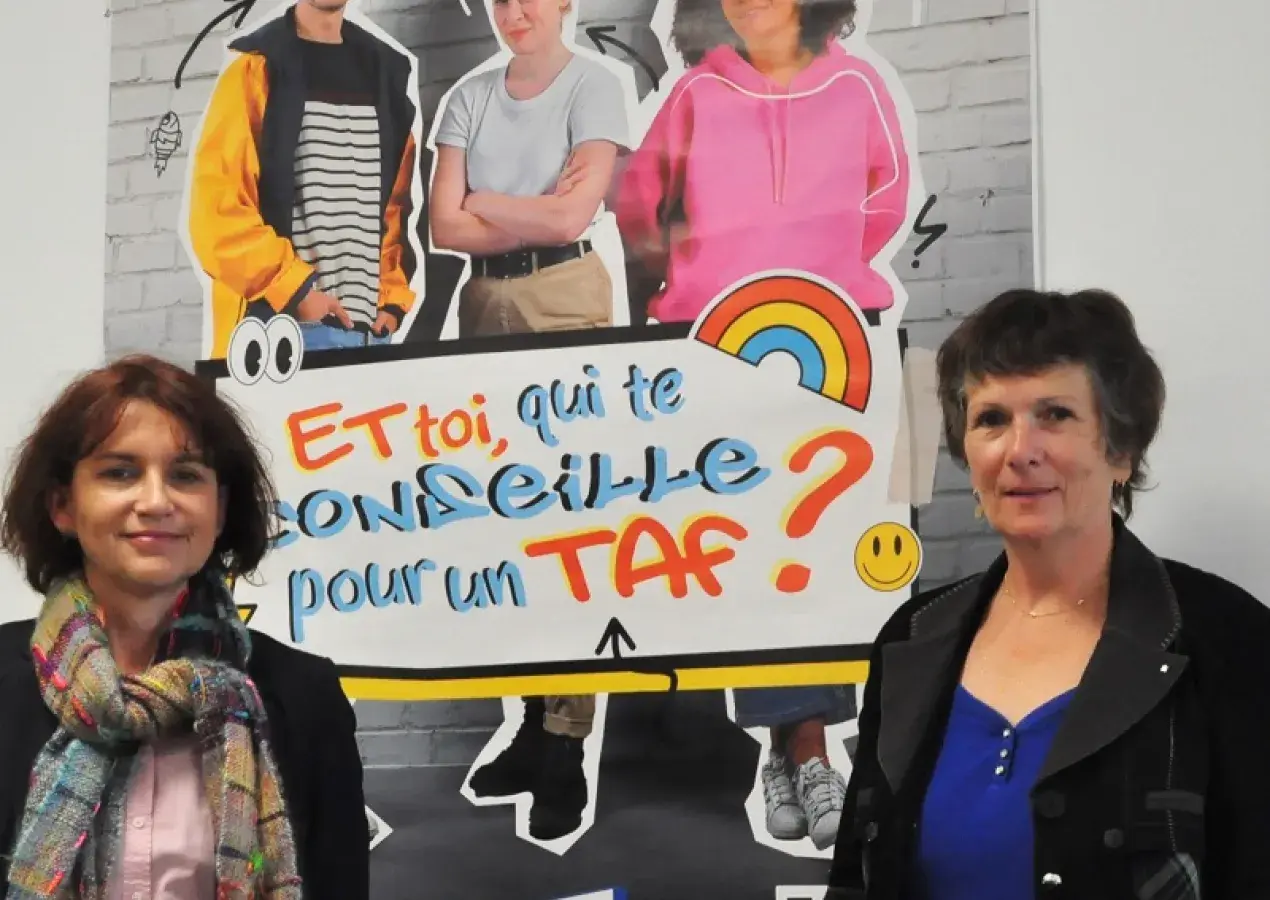 Deux femmes posent autour d'une affiche de la Mission locale du Pays de Brest. 