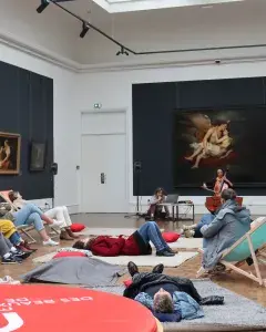 ¨Photos montrant des personnes assises dans une salle d'exposition de peintures d'un musée, en train d'écouter une violoncelliste jouer un concert.