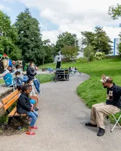 Une personne assise lit des livres à hautes voix pour des enfants dans un parc