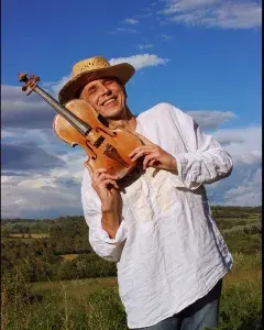 Photo montrant un homme souriant dans un champ avec un violon posé contre sa joue.