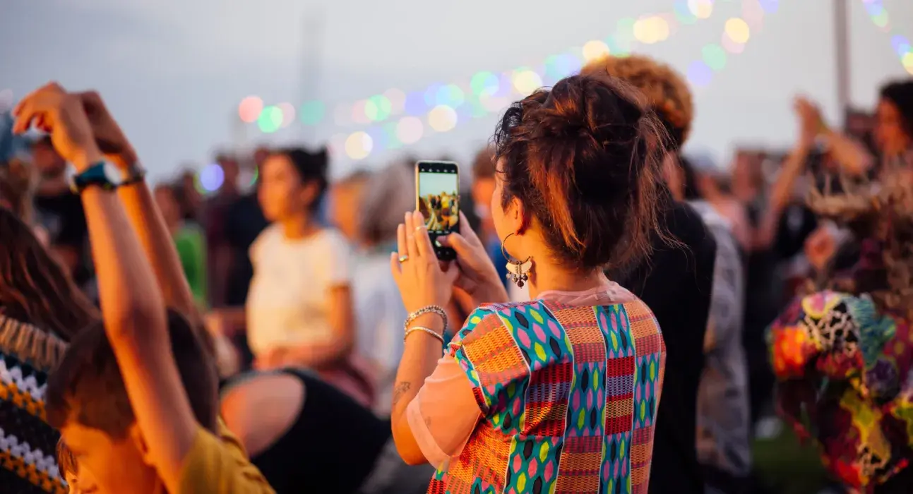 Une jeune femme dans une foule, qui filme un spectacle avec son portable
