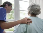 Une infirmière se penche en souriant vers une personne âgée 