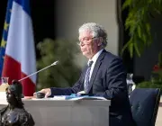 Un homme au micro devant un drapeau français.