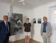 Trois personnes posent devant des photos. 