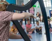 Une femme joue de la harpe devant des enfants. 