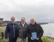 Trois hommes posent devant un bâtiment militaire. 