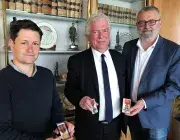Trois hommes montrent les médailles attribuées à la ville de Brest suite à la Seconde Guerre mondiale