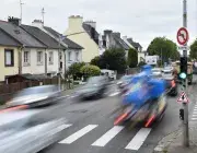 Des voitures passent à grande vitesse à côté d'habitations. 