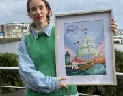 Une femme debout tient un cadre avec l'affiche des Fêtes maritimes de Brest 2027.