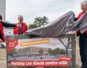 Trois hommes lèvent un voile sur un mur en pierres. 