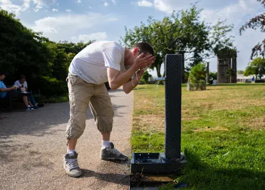Une personne boit de l'eau à un robinet public