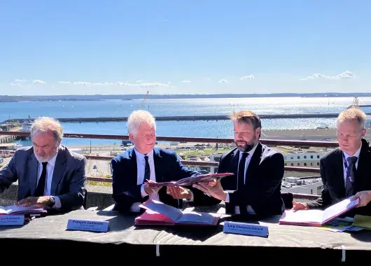 Des hommes signent un document officiel sur le parvis de la gare de Brest, au-dessus du port