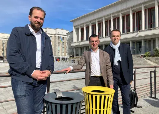 Trois hommes posent à côté de nouvelles corbeilles de tri des emballages, place de la Liberté