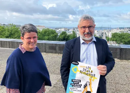 Un homme et une femme posent avec l'affiche de l'opération des Lieux à réinventer de la ville de Brest. 