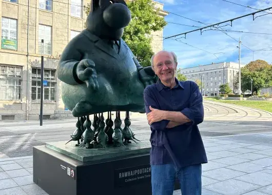 Philippe Geluck debout devant une de ses statues du Chat.