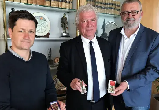 Trois hommes montrent les médailles attribuées à la ville de Brest suite à la Seconde Guerre mondiale