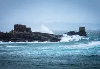 Des vagues déferlent sur des rochers.