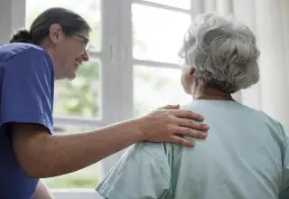 Une infirmière se penche en souriant vers une personne âgée 