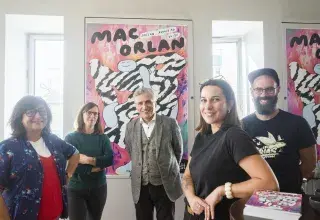 Cinq personnes posent devant une affiche.