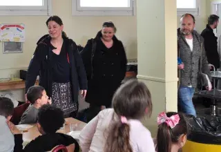 Des enfants assis à la cantine et des adultes autour leur parlant