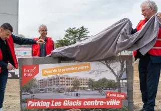 Trois hommes lèvent un voile sur un mur en pierres. 