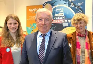 Un homme entouré de deux femmes, devant l'affiche présentant le campus mondial de la mer