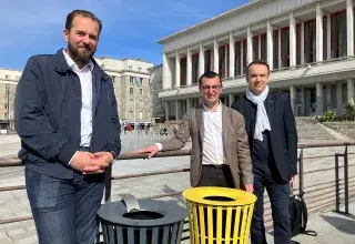 Trois hommes posent à côté de nouvelles corbeilles de tri des emballages, place de la Liberté