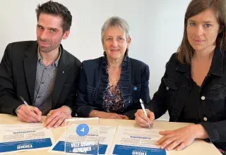 Un homme et deux femmes signent une charte d'engagement. 