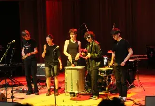 Photo montrant un groupe d'étudiantes et étudiants jouant un concert de rock sur scène avec des percussions et de la guitare